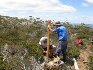 Two men installing a marker pole in the bush